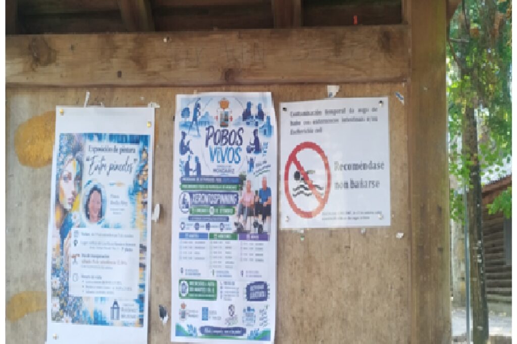 Único cartel de advertencia sanitaria localizado en la zona, junto al aparcamiento de O Val y alejado de la orilla, compartiendo tablón con anuncios ajenos a la calidad del agua (19/09/2026).